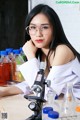 A woman wearing glasses sitting at a table with a microscope.