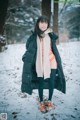 A woman standing in the snow wearing a black coat.