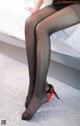 A woman wearing black stockings and high heels sitting on a bed.