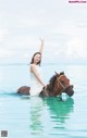 A woman riding on the back of a brown horse in the ocean.