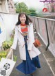 A woman in a white coat and blue skirt holding a bag.