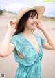 A woman in a blue dress and a straw hat on the beach.