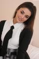 A woman in a white shirt and black tie sitting on a bed.