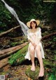 A woman sitting on a log in front of a waterfall.